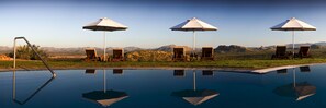 Ein Pool mit klarem Wasser, das die umliegende Landschaft spiegelt, Holzliegen und Sonnenschirme.