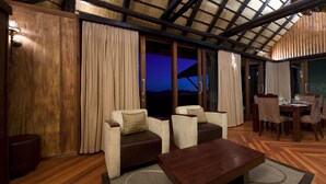 A cozy room with a wooden ceiling, a dining area with a table and chairs, and a large window with curtains.