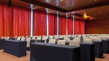 A conference room with rows of tables, chairs, and a red curtain backdrop.
