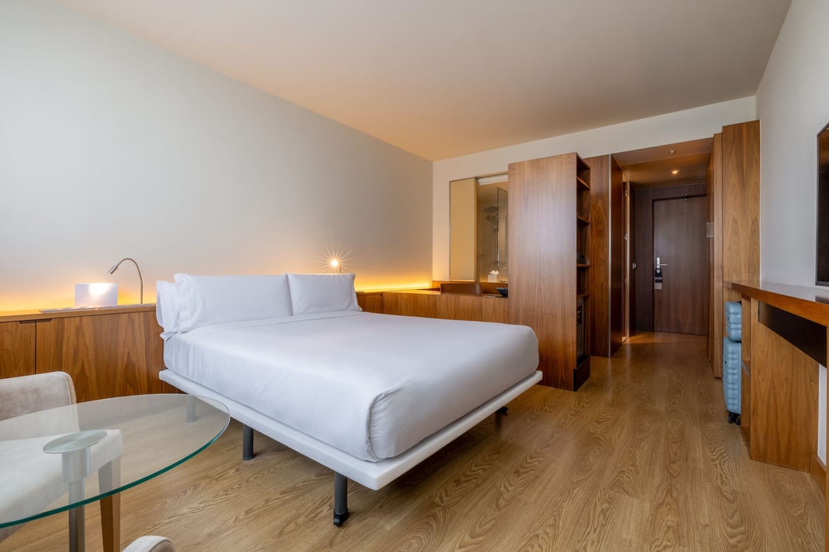 Une chambre d’hôtel moderne comprenant un lit, une table en verre, une chaise, un bureau et un miroir.