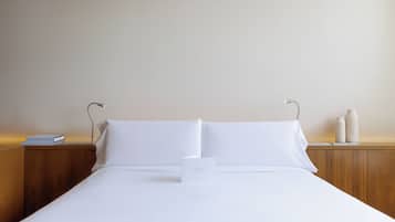 Ein ordentlich bezogenes Bett mit weißen Leinen, ein kleiner Nachttisch mit einem Buch und einer Lampe sowie ein Beistelltisch mit einer Vase.