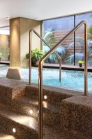 Uma área de piscina com escadas dando acesso à água, corrimãos de metal e plantas em vasos.