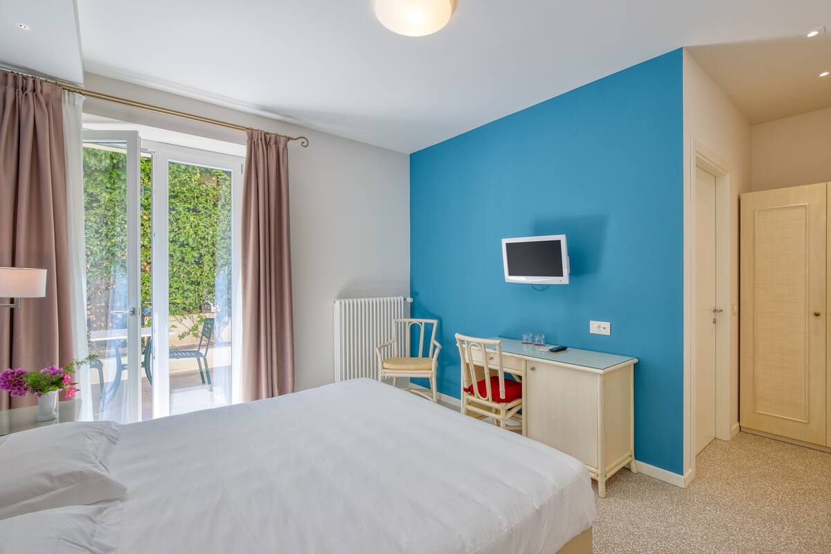 Ein Schlafzimmer mit Bett, Schreibtisch, Stuhl, Fernseher und Blick ins Freie.