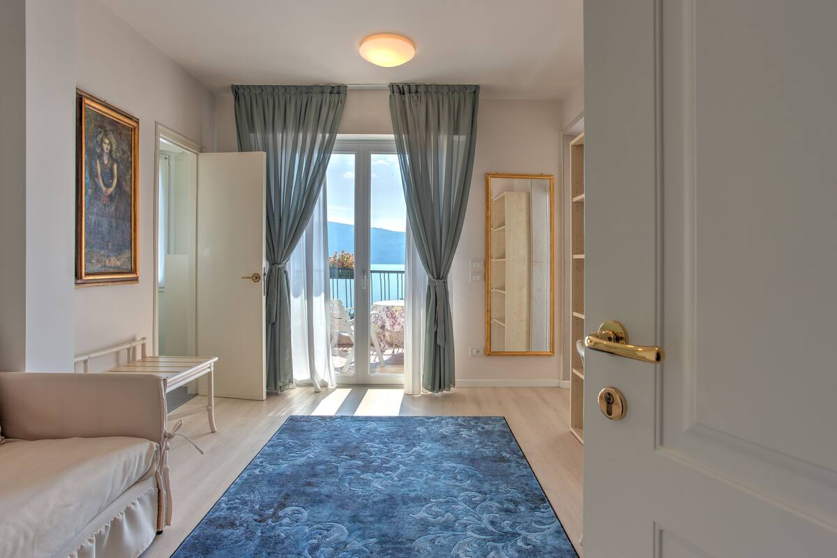 Ein Hotelzimmer mit großem Fenster, einem blauen Teppich mit Muster, einem weißen Sofa und einem Spiegel an der Wand.