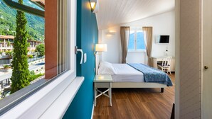Habitación de hotel con cama, una mesita, lámpara, televisor y ventana con vista a una montaña y edificios.