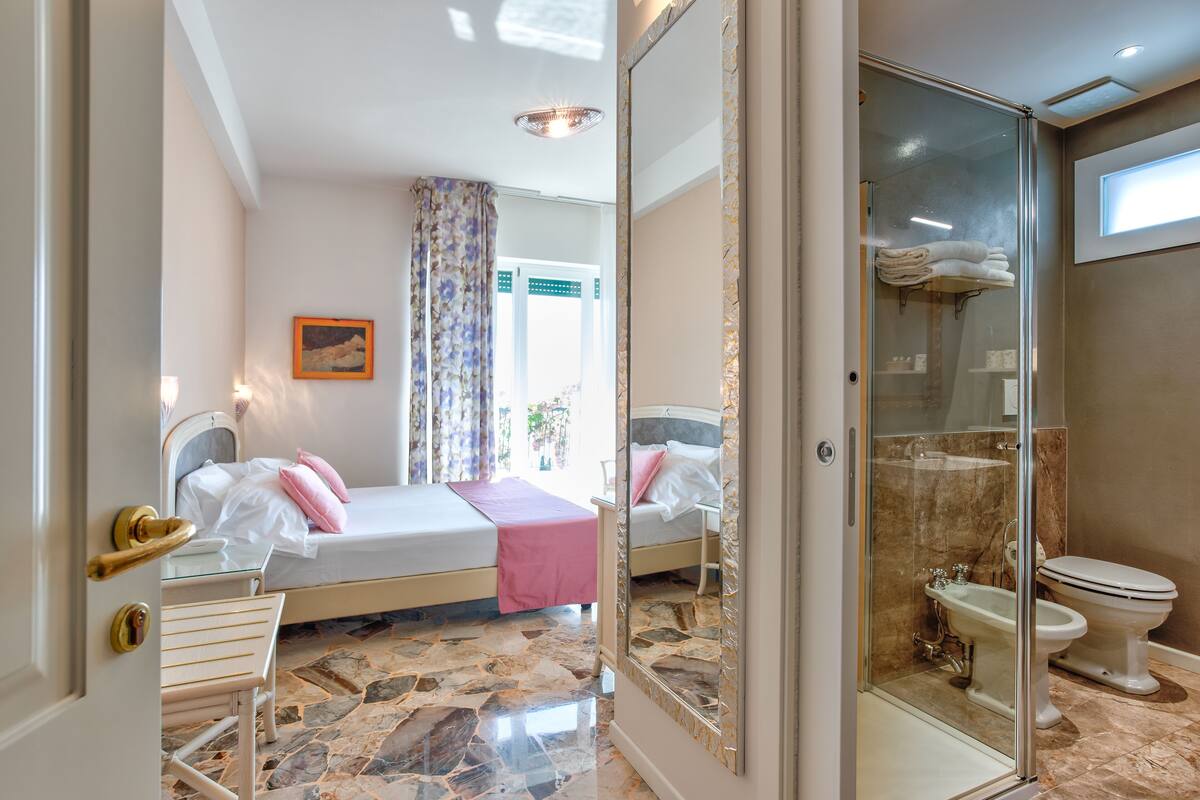 Ein Hotelzimmer mit zwei Betten, einem Badezimmer mit Duschkabine aus Glas und einem Marmorboden.