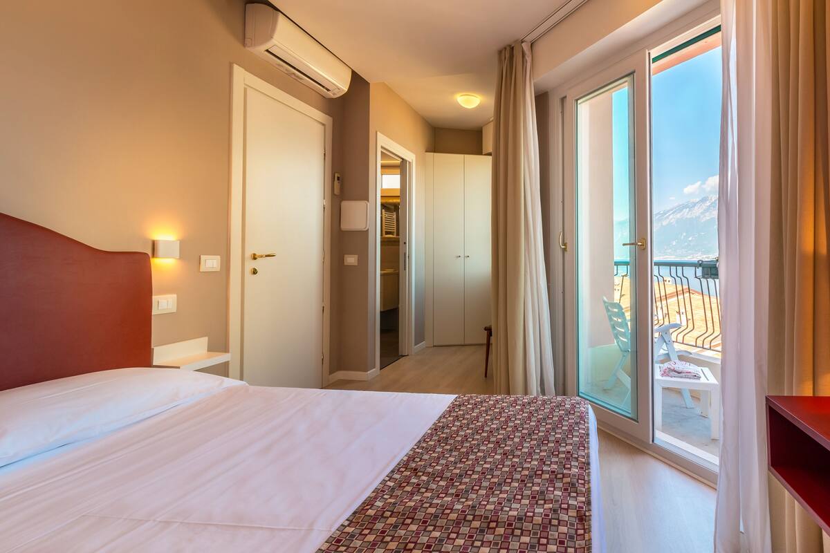 Ein Hotelzimmer mit Bett, Schrank, Badezimmer und einem Balkon mit Bergblick.