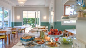 Comedor con mesas y sillas, una araña y un bufé con diferentes alimentos.