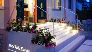 Entrada de un hotel con una escalera, un letrero que dice "Hotel Villa Europa" y un interior bien iluminado visible a través de puertas de vidrio.