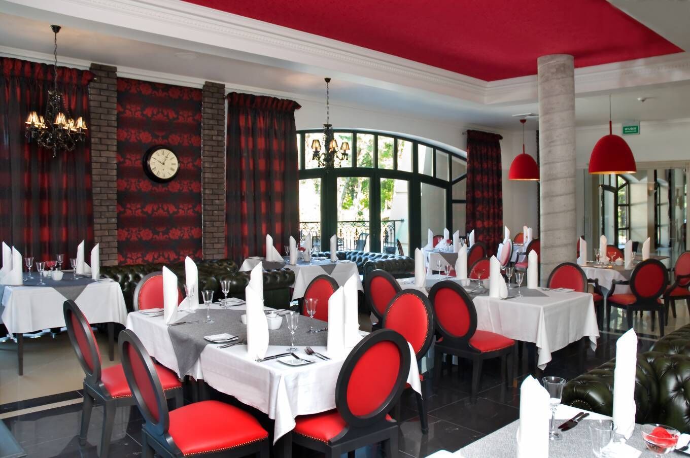 Ein Restaurant mit gedeckten Tischen, rot gepolsterten Stühlen und einer großen Wanduhr.