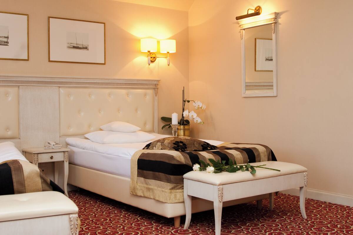 A hotel room with a large bed, a bedside table with a lamp, a mirror, and artwork on the wall.