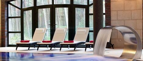 A spa area with a pool, lounge chairs, and a waterfall feature.