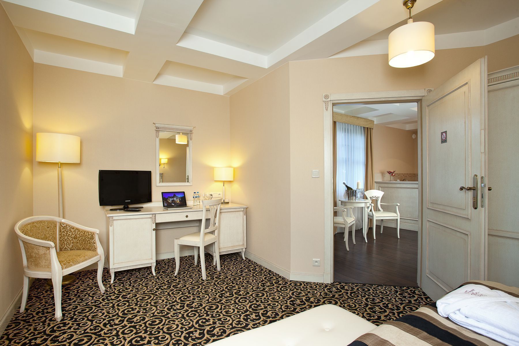A hotel room with a bed, a desk with a laptop, a chair, a television, and a mirror.