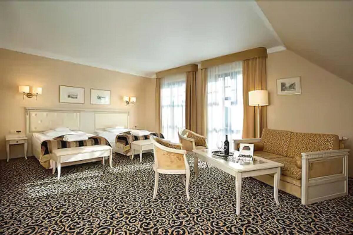 A hotel room with a bed, two chairs, a sofa, a small table, and a lamp.