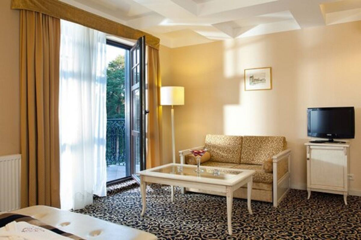 A hotel room with a sofa, a coffee table, a television, and a view of the outdoors.