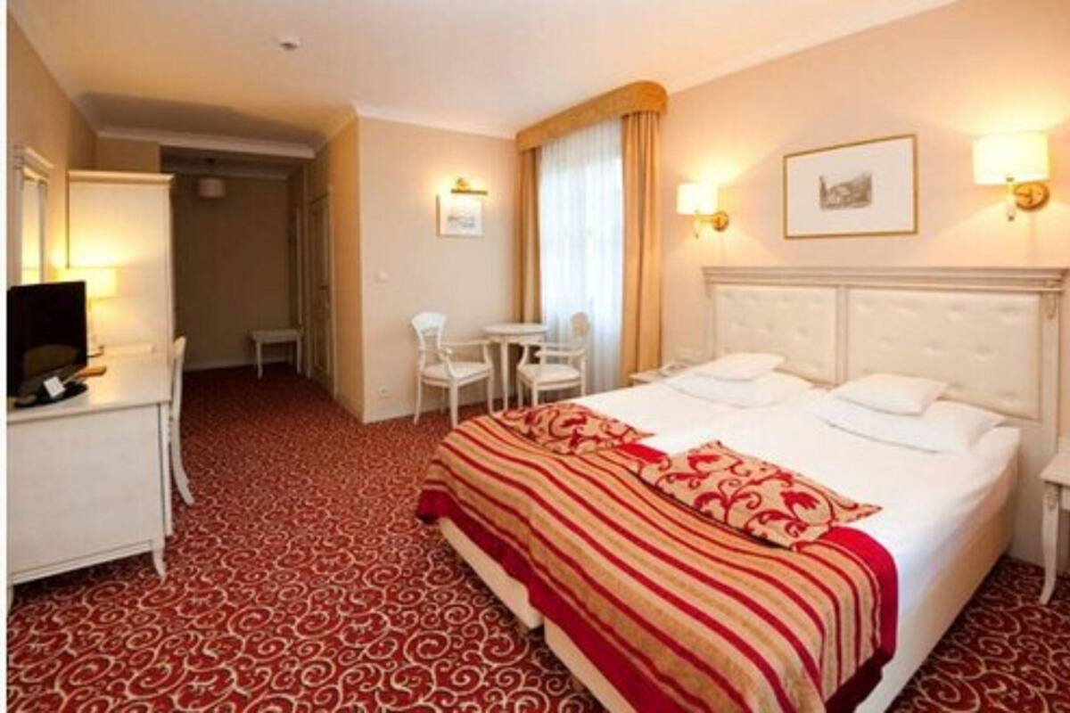 A hotel room with a large bed, a desk with a chair, a small table, and a television.
