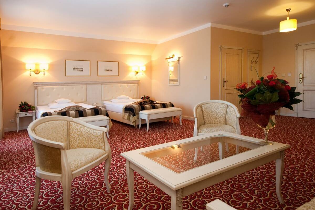 A hotel room with two beds, a sitting area with chairs, a table, and a large vase of flowers.