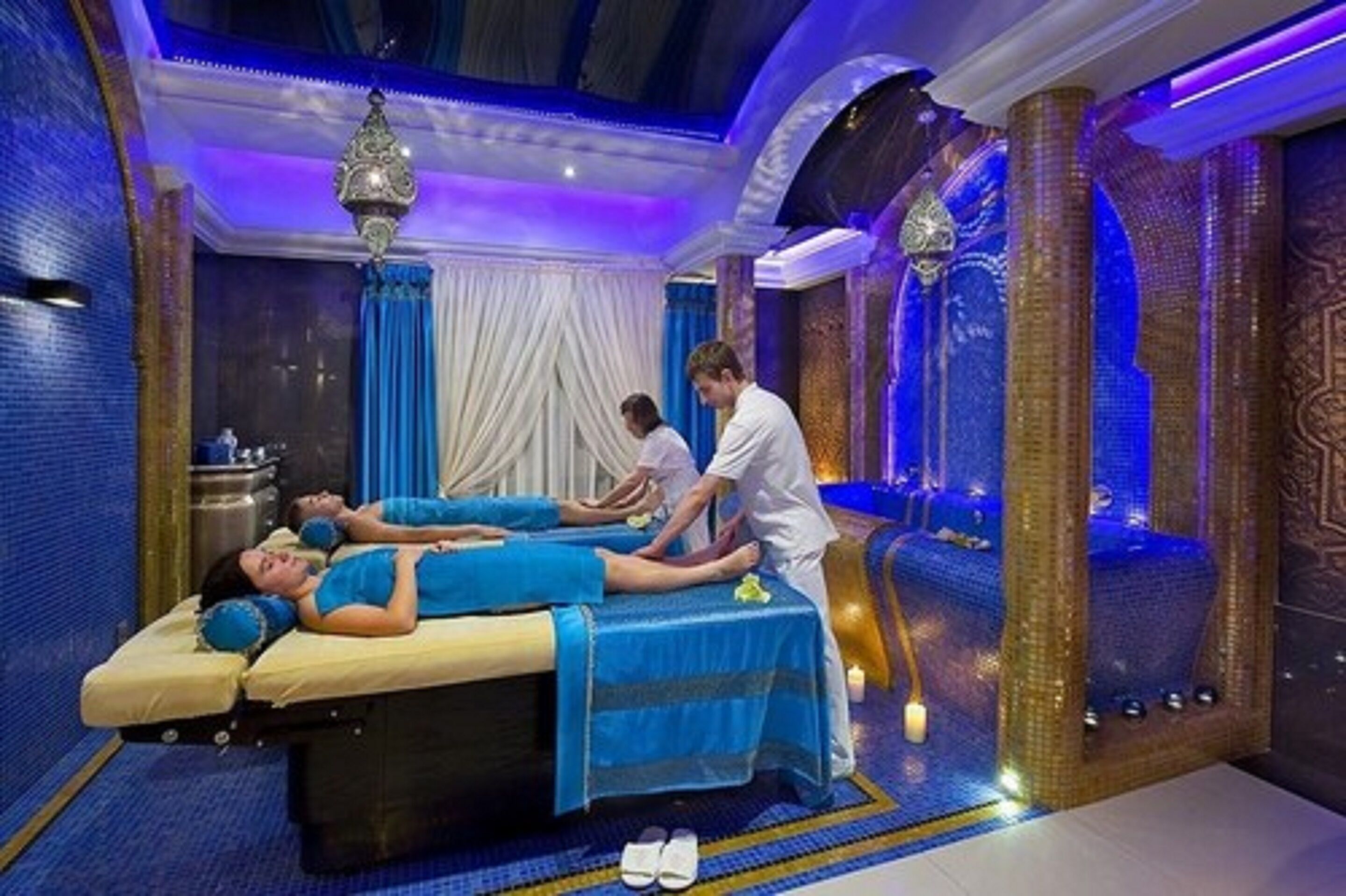 A massage therapy room with two massage tables, a massage therapist, and a decorative wall with a blue and gold color scheme.