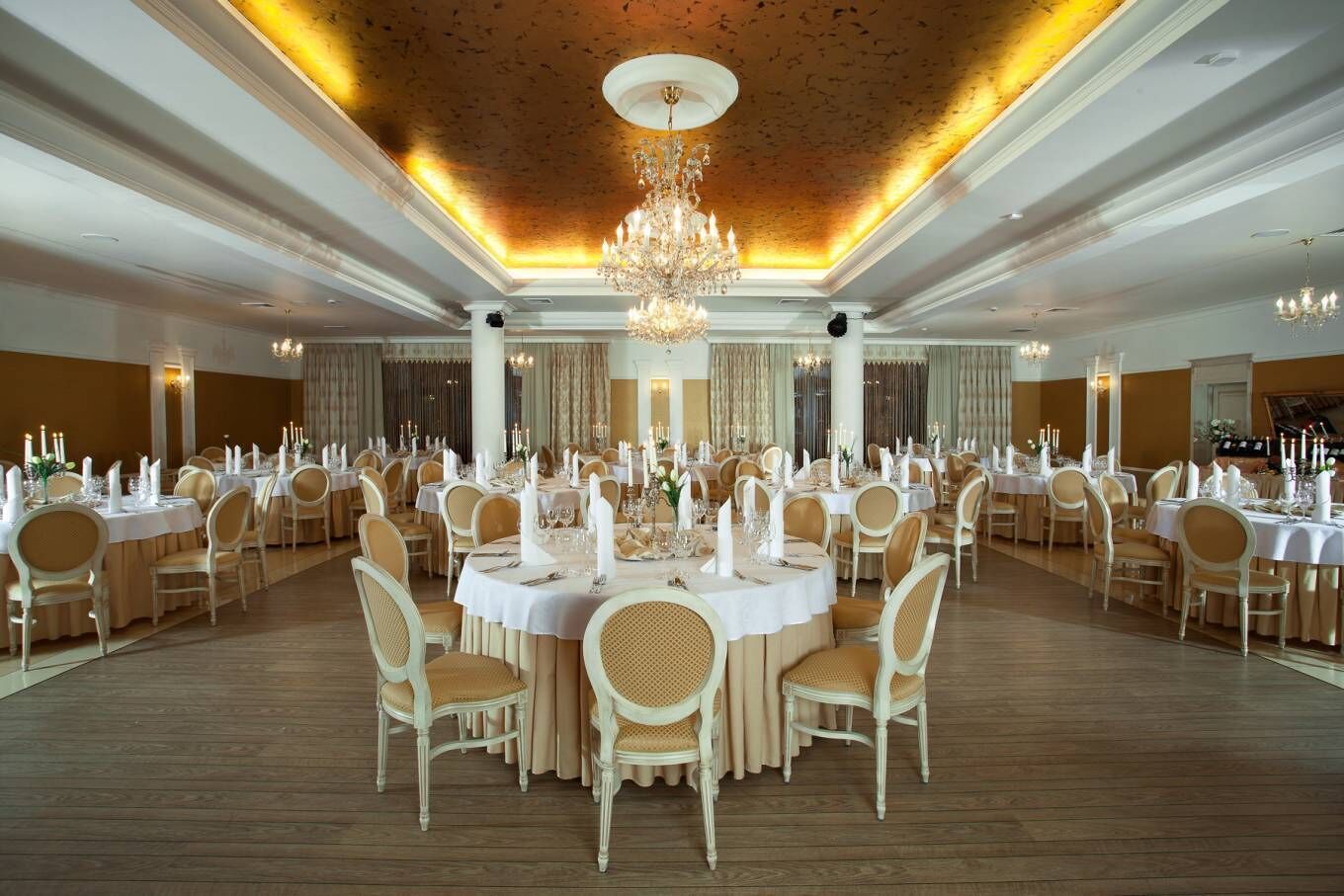 A banquet hall with round tables, white tablecloths, and chandeliers.