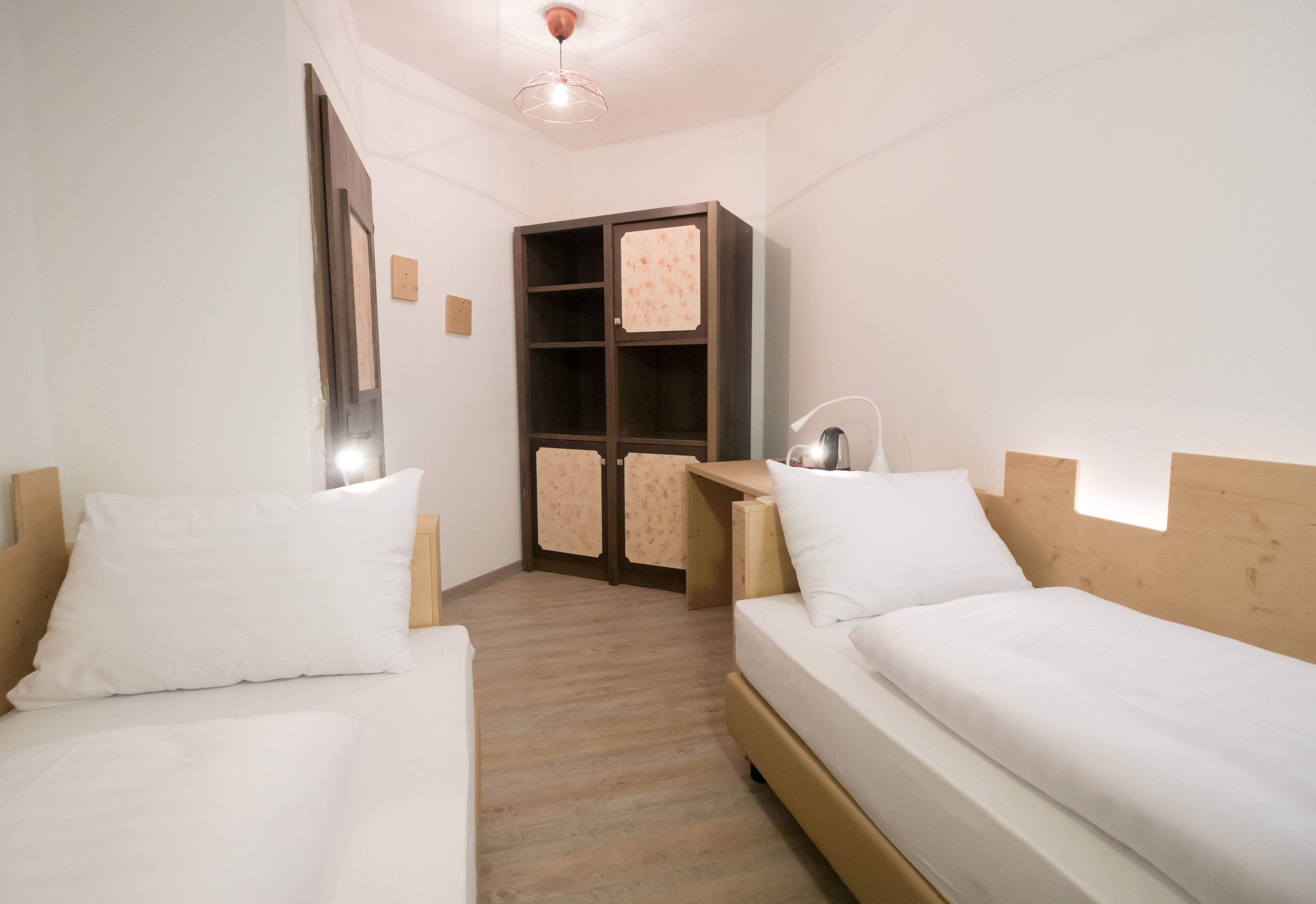 A bedroom with two beds, a wooden headboard, a nightstand, a desk, and a wardrobe.