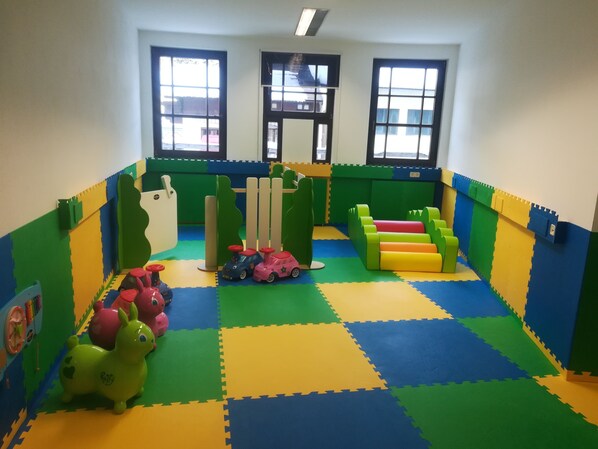 A play area with colorful foam mats, a green and yellow play structure, and toy cars.
