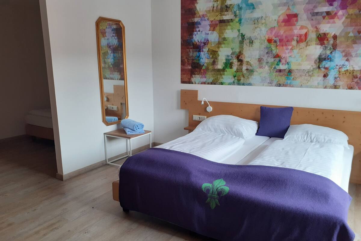 Una habitación de hotel con una cama, una mesita de noche, un espejo y un cuadro abstracto grande en la pared.