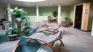A sunlit indoor relaxation area with lounge chairs, potted plants, and a wooden table. - Schlosshotel Rosenegg (Fieberbrunn)