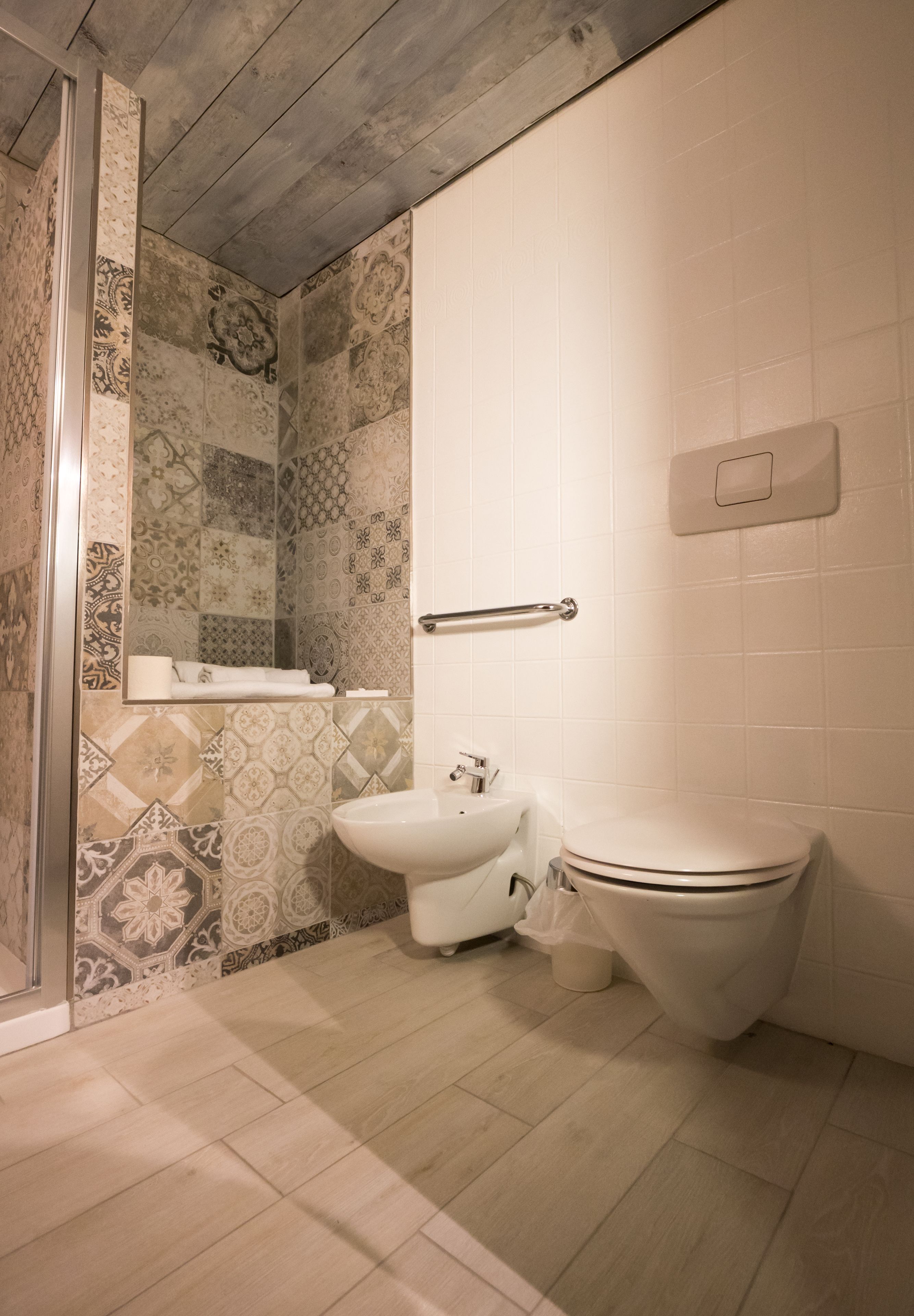 Ein Badezimmer mit Dusche, Toilette und Waschbecken, ausgestattet mit gemusterten Fliesen und einer Holzbalkendecke.