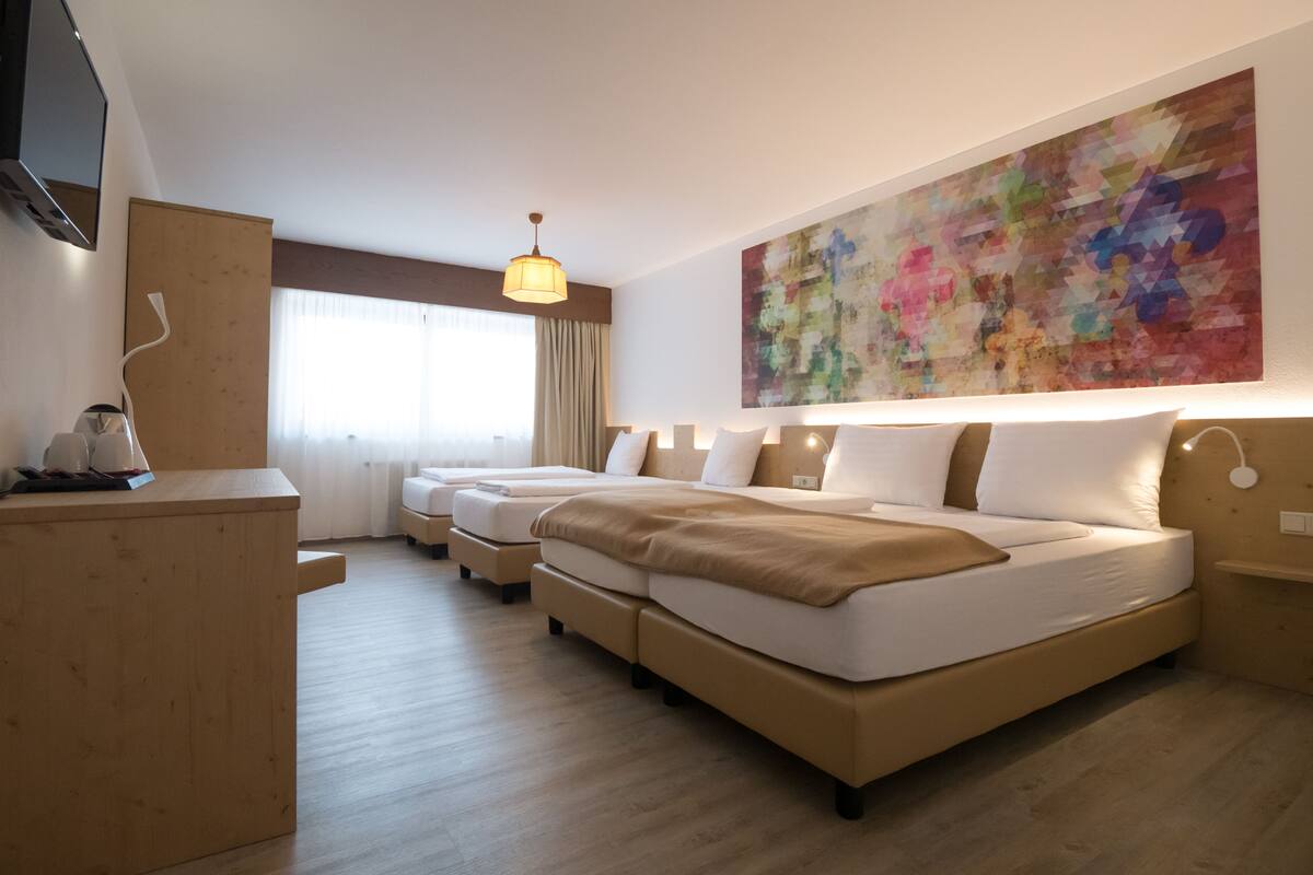 Una habitación de hotel con una cama grande, dos camas más pequeñas, un escritorio y un televisor.