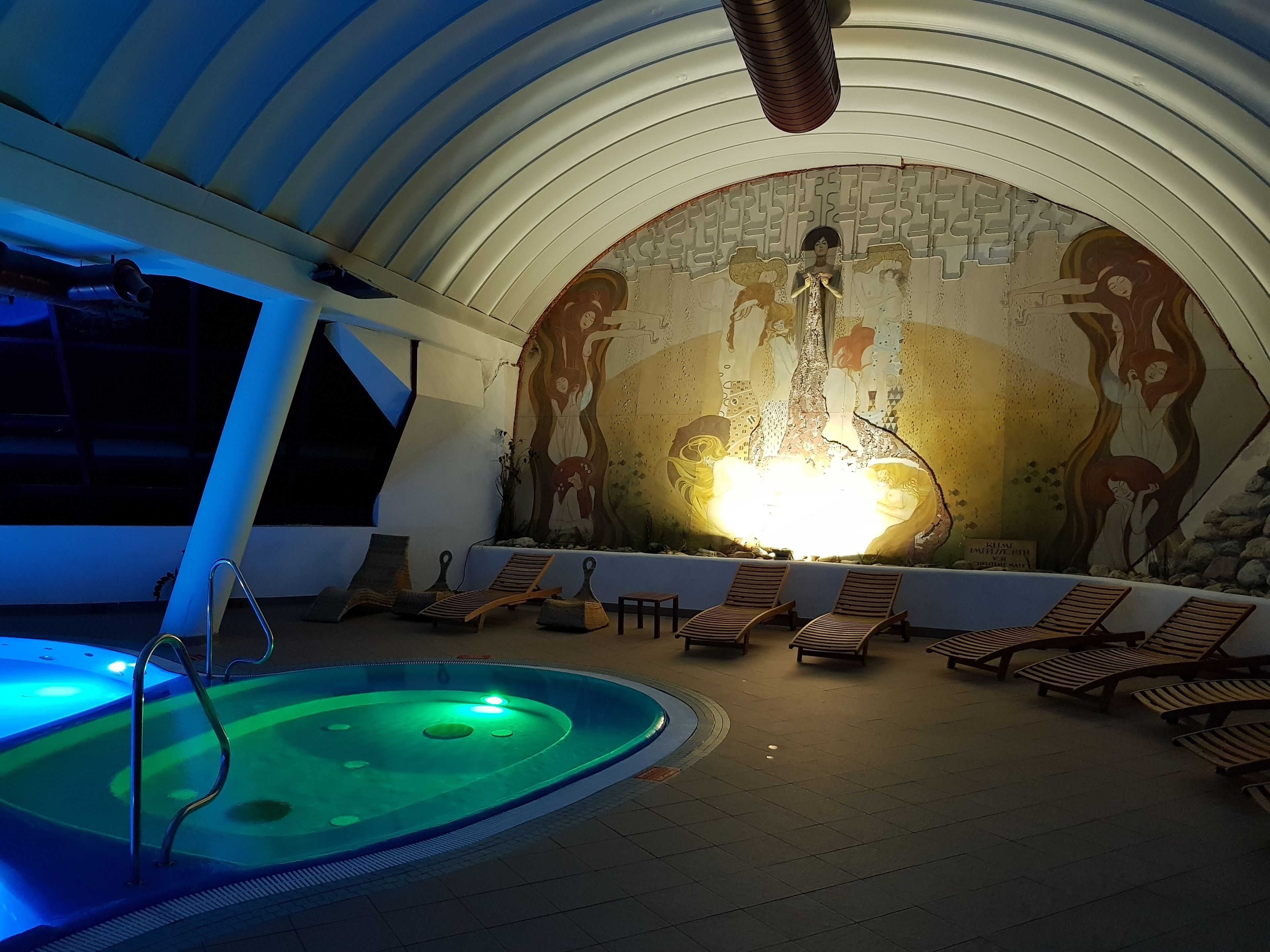 Ein Wellnessbereich mit Whirlpool, Liegestühlen und Wandgemälde.