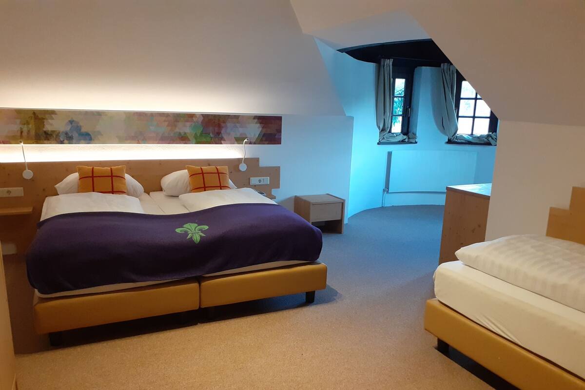 Un dormitorio con una cama grande, una cama más pequeña, una mesita de noche, un aparador y una ventana con cortinas.
