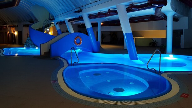 A swimming pool area with a blue-lit design, a lifebuoy, and a curved seating area. - Schlosshotel Rosenegg (Fieberbrunn)