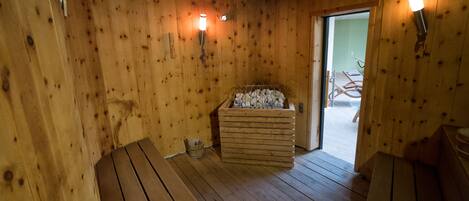 A sauna room with wooden walls, a bench, a wooden bench, a sauna heater, and a wooden door.