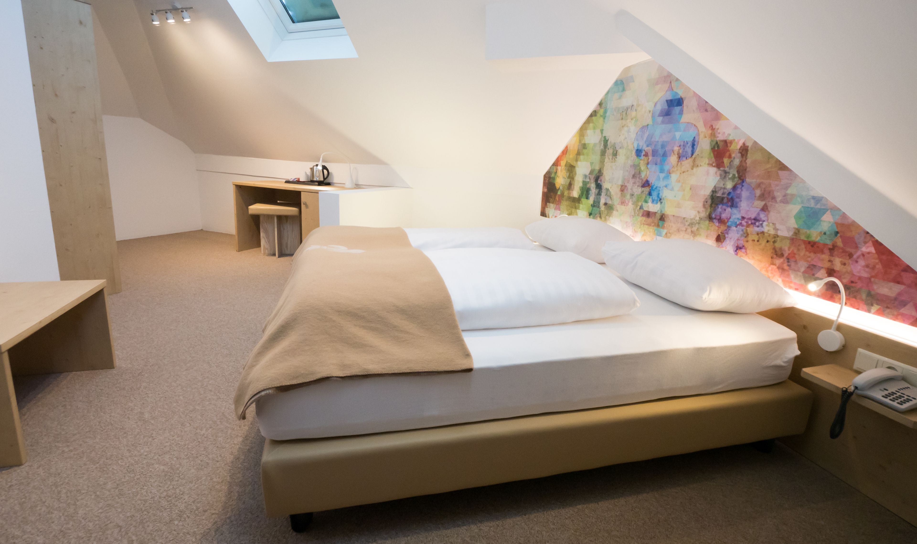 Une chambre moderne avec un lit, un bureau et une œuvre d’art murale aux couleurs vives.