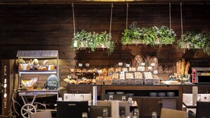 A café with wooden walls, hanging plants, and a variety of baked goods and beverages displayed on shelves and counters. - Hotel Val De Neu (Naut Aran)