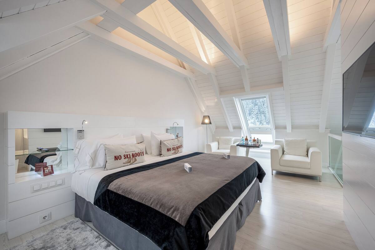 A bedroom with a large bed, a bedside table, a chair, a desk, and a window.