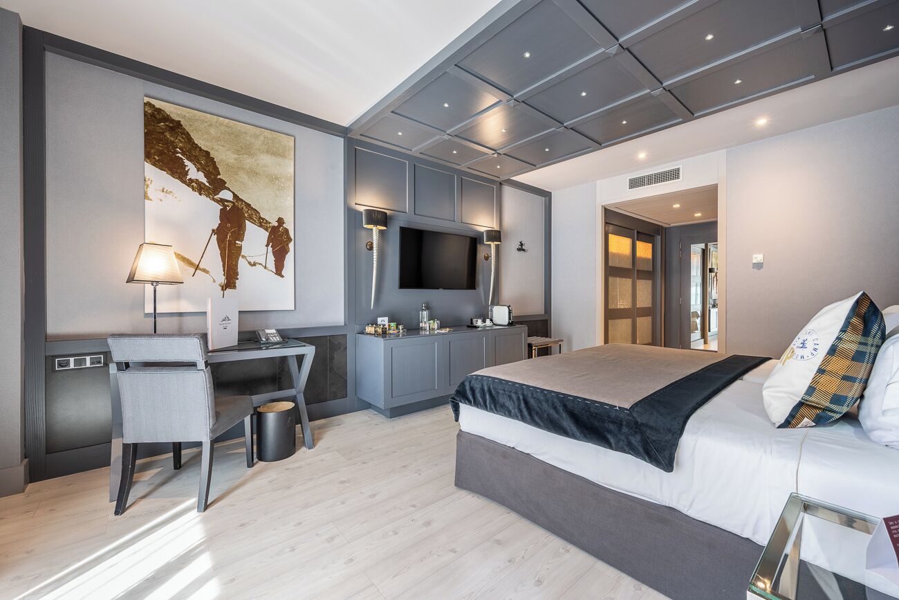 A modern hotel room with a large bed, a desk, a flat-screen TV, and a large artwork on the wall.