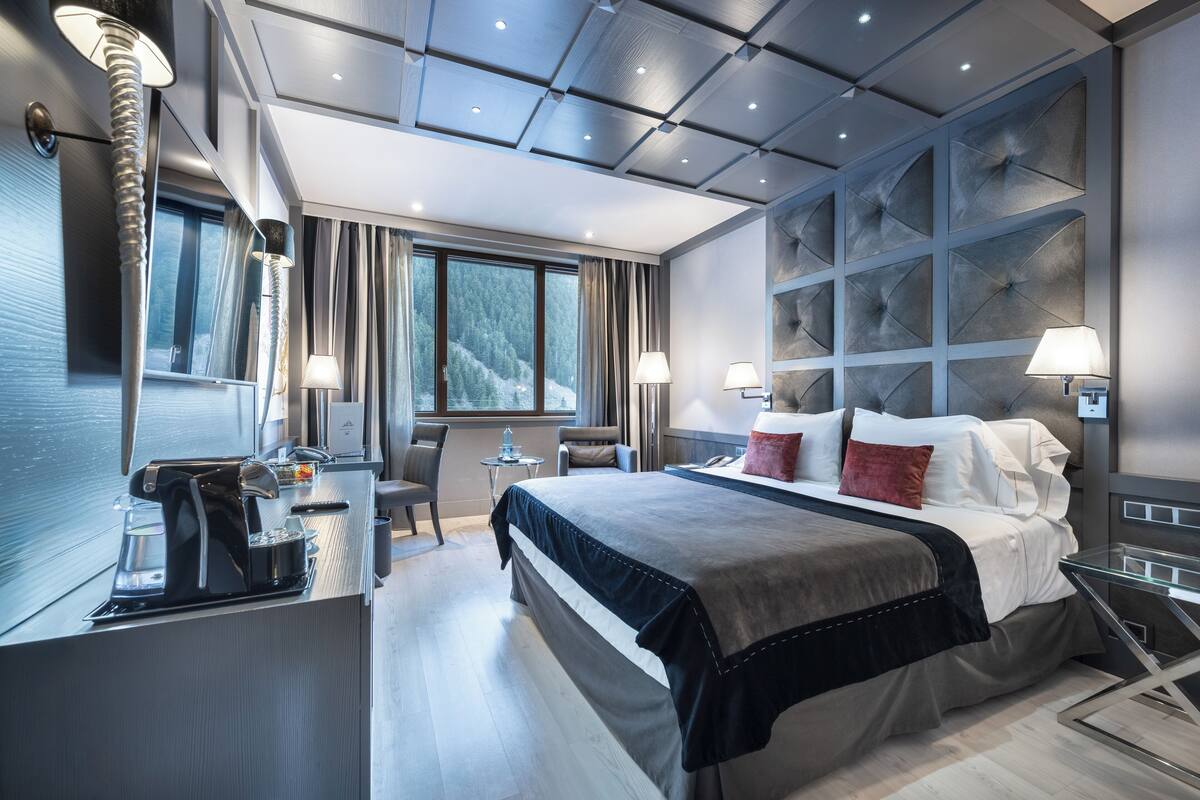 A modern hotel room with a large bed, bedside lamps, a coffee machine, and a view of the mountains.
