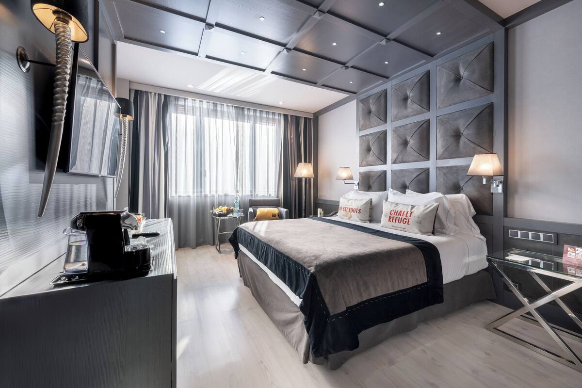 A modern hotel room with a large bed, a desk with a coffee maker, and a glass side table.