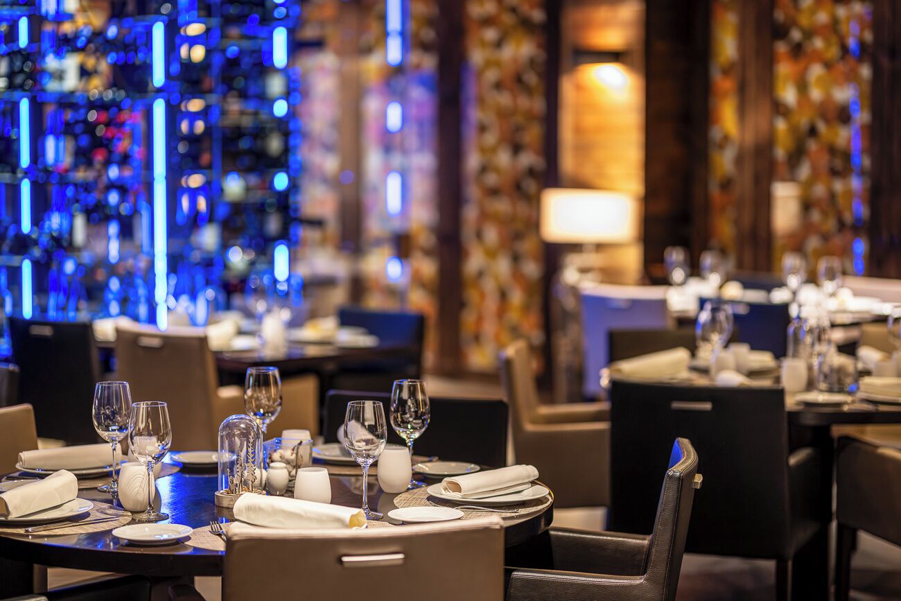 Un restaurante con mesas dispuestas para comer, con una decoración moderna que incluye detalles de iluminación azul y una pared decorativa.