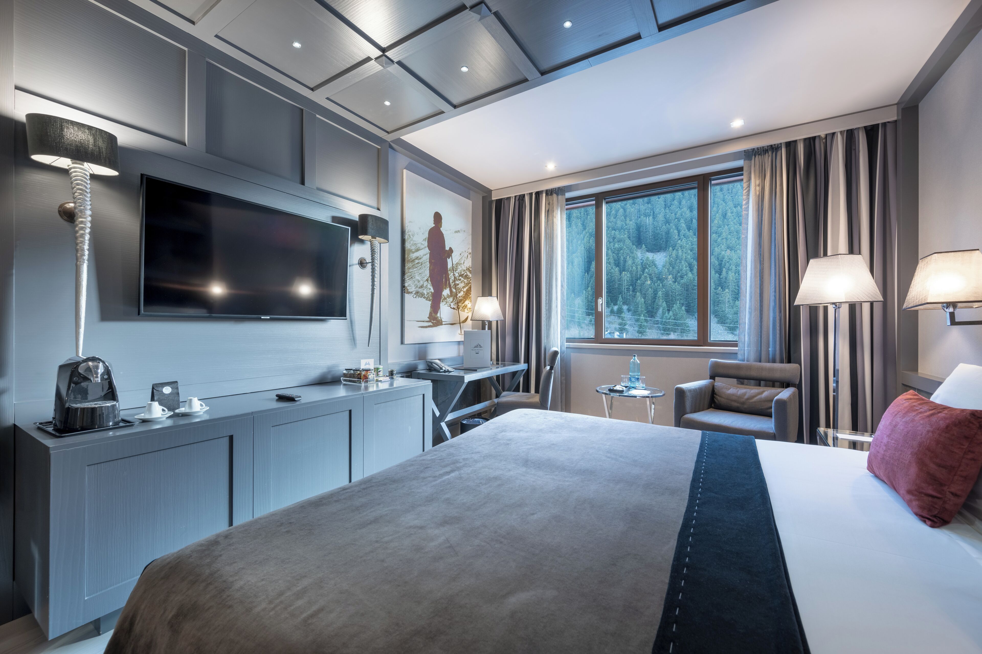 Een moderne hotelkamer met een groot bed, een bureau, een flatscreen-televisie en een raam met uitzicht op een bos.