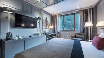 Een moderne hotelkamer met een groot bed, een bureau, een flatscreen-televisie en een raam met uitzicht op een bos.