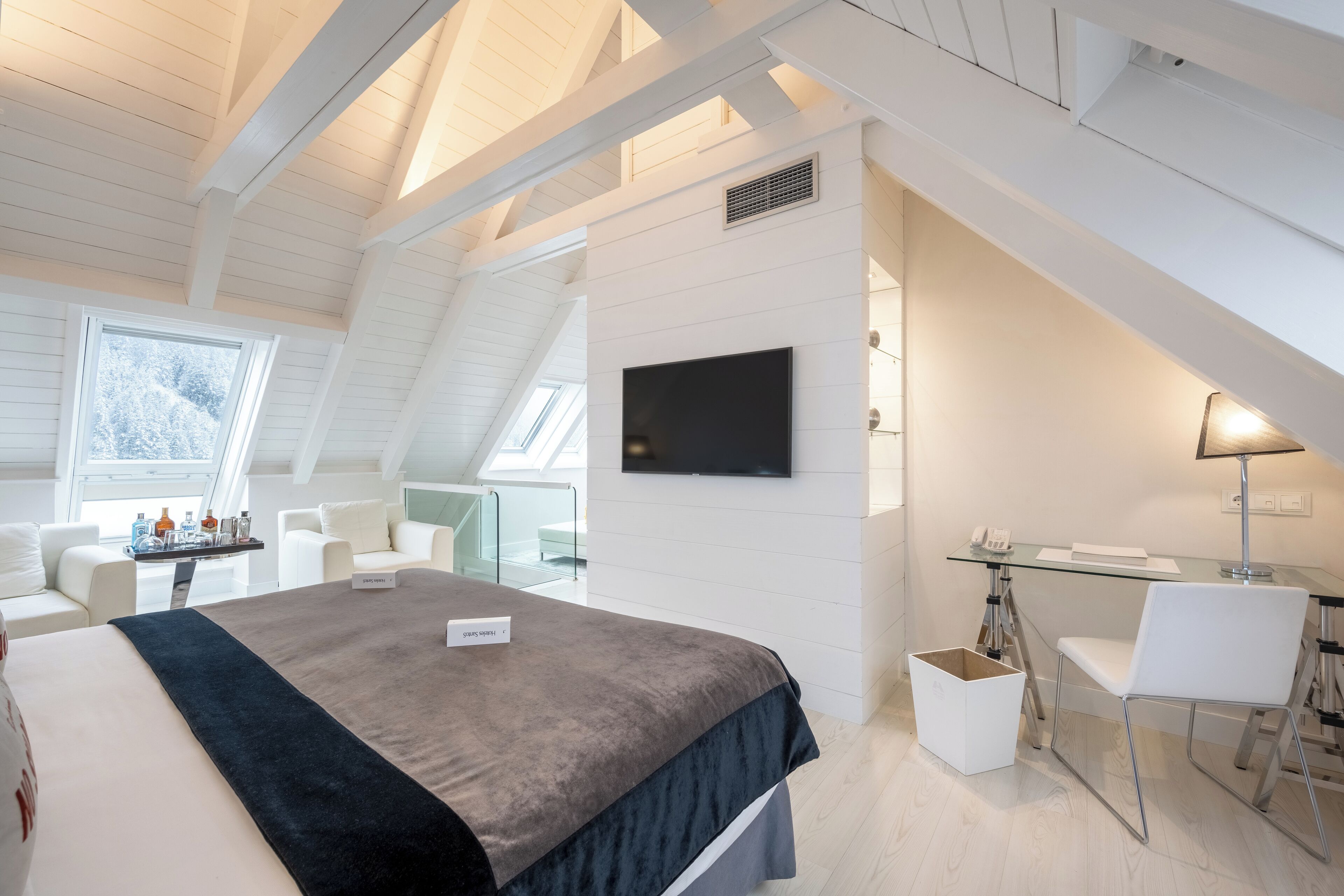 Una habitación de hotel moderna con una cama grande, un escritorio y un televisor en la pared.