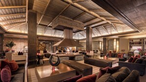 A spacious lounge area with high ceilings, wooden beams, and a central fire feature. - Hotel Val De Neu (Naut Aran)