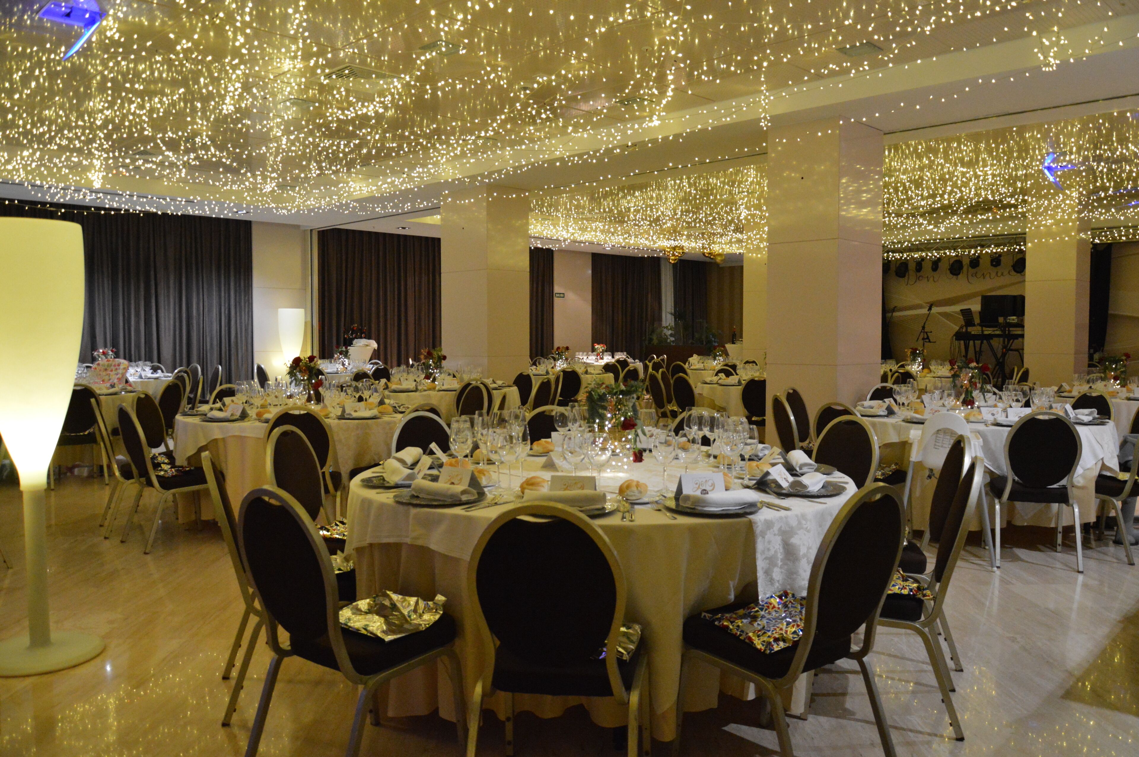 Una sala da banchetti con tavoli rotondi apparecchiati per la cena, con lampadari e luci a catena.