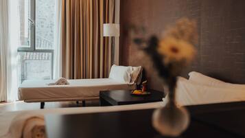 Een hotelkamer met een bed, een nachtkastje met een lamp en uitzicht door een raam.