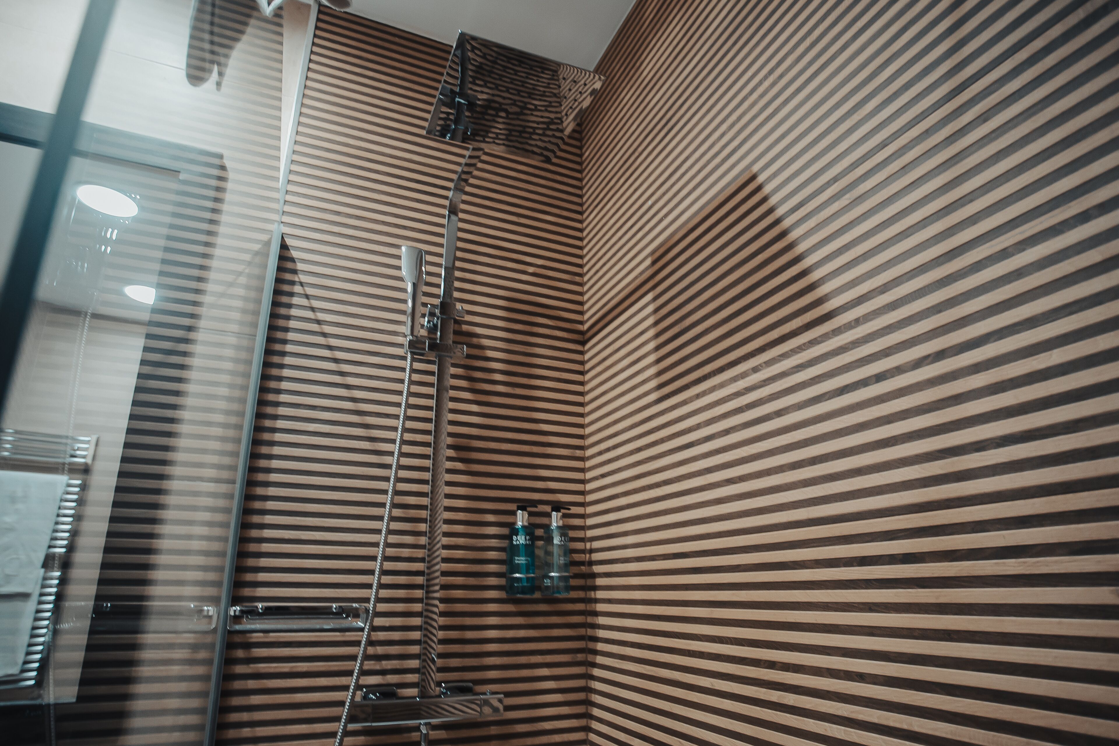 A bathroom with striped wooden walls, a glass shower enclosure, and two bottles of shampoo.