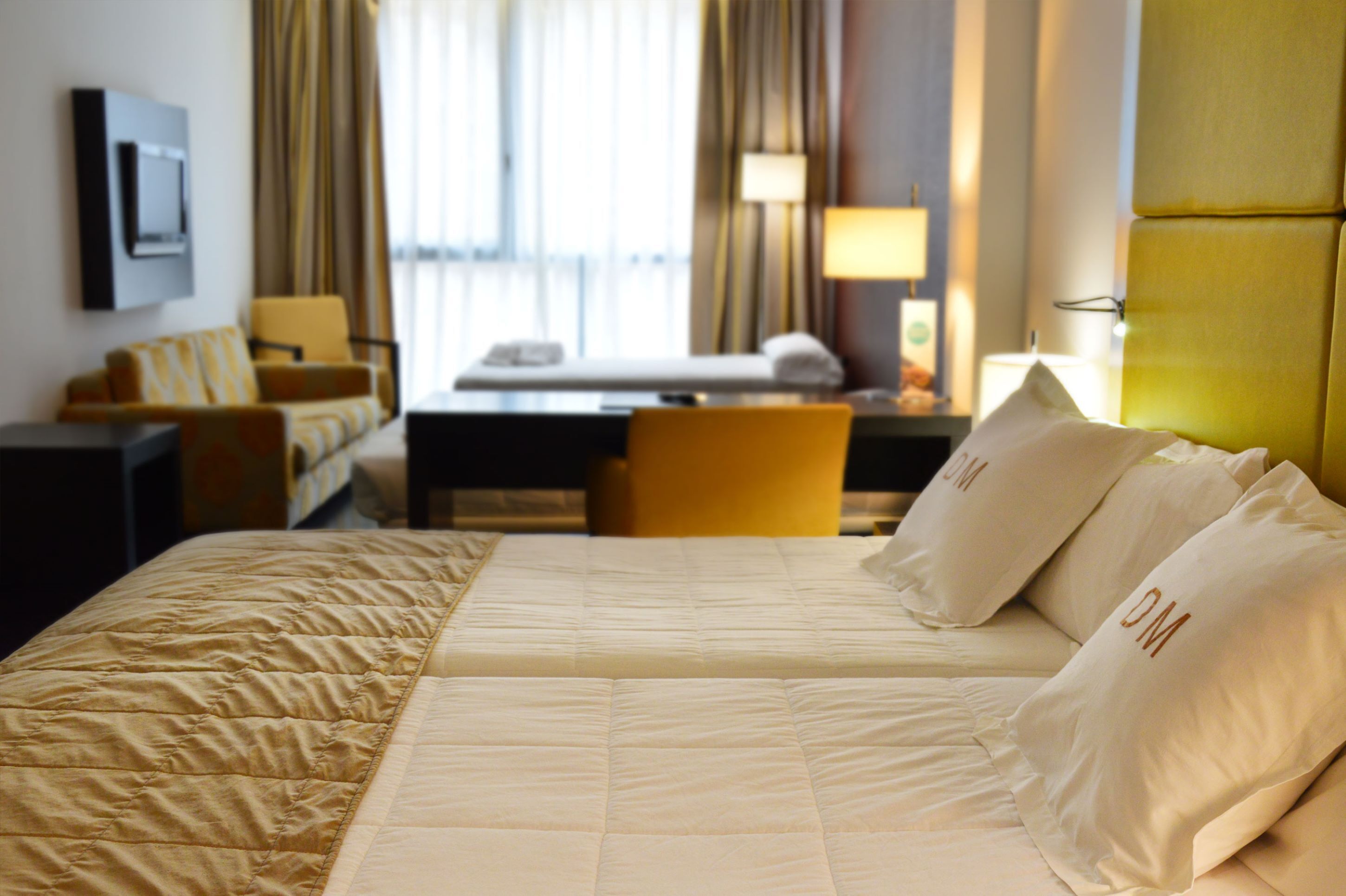 A hotel room with a large bed, a desk, a chair, and a sofa.