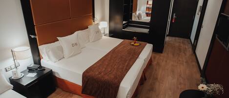 Habitación de hotel con una cama grande, una mesita de noche con lámpara, una pequeña mesa con un florero y un espejo en la pared.