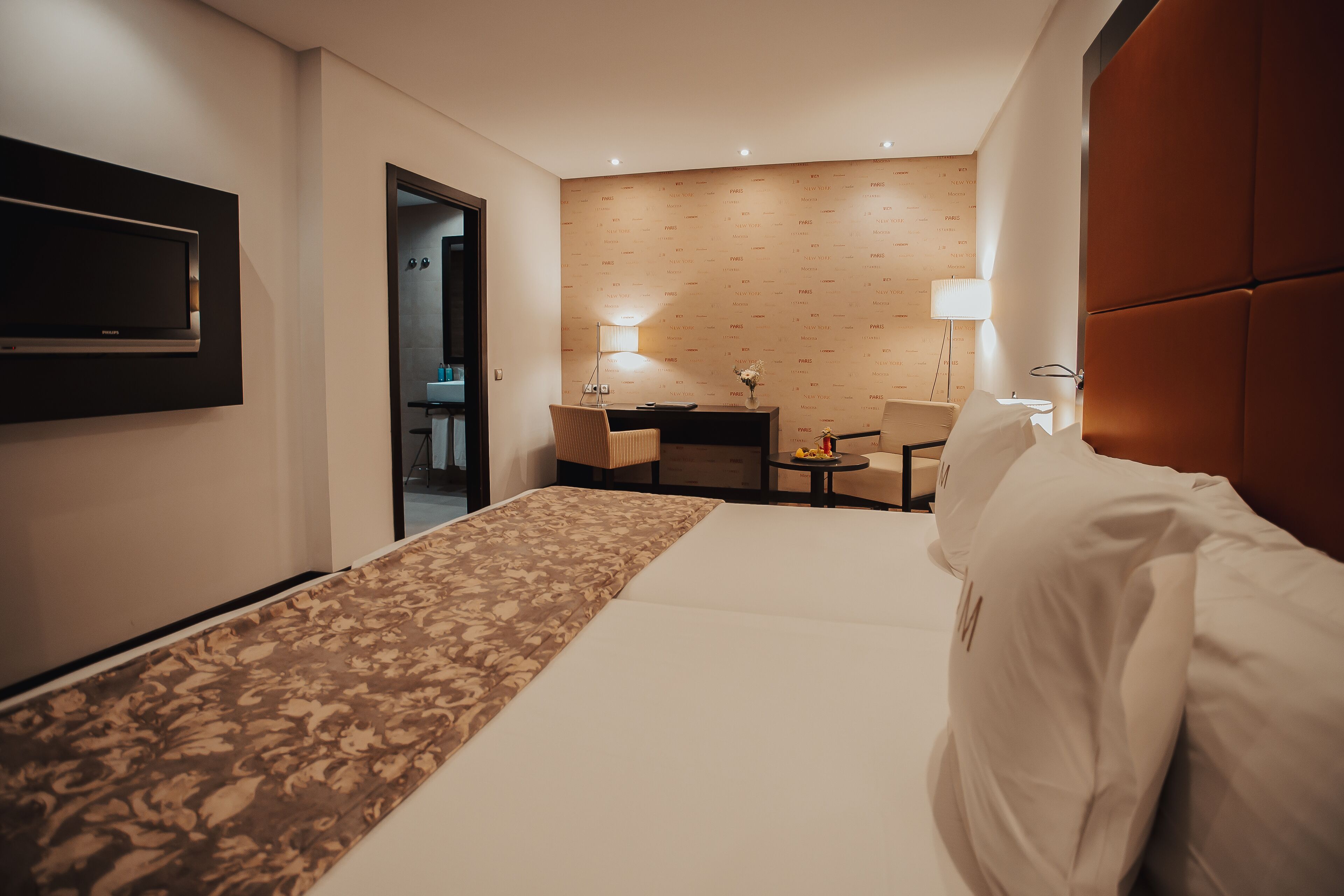 Habitación de hotel con cama, escritorio, dos sillas, televisor y lámpara.